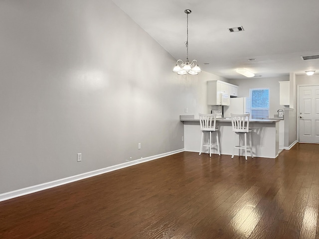 unfurnished living room featuring baseboards, dark wood-style flooring, visible vents, and a notable chandelier