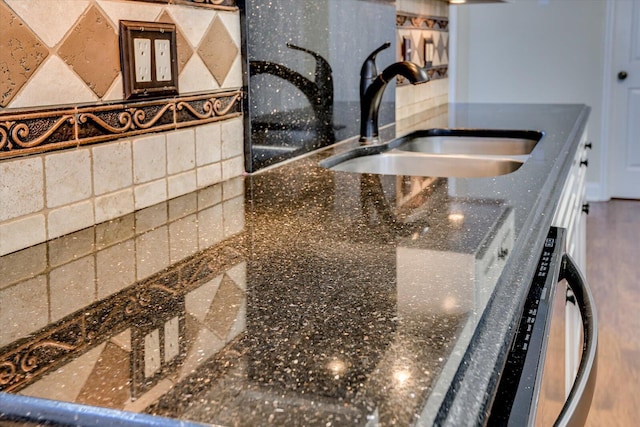 room details featuring sink, decorative backsplash, and dark stone countertops