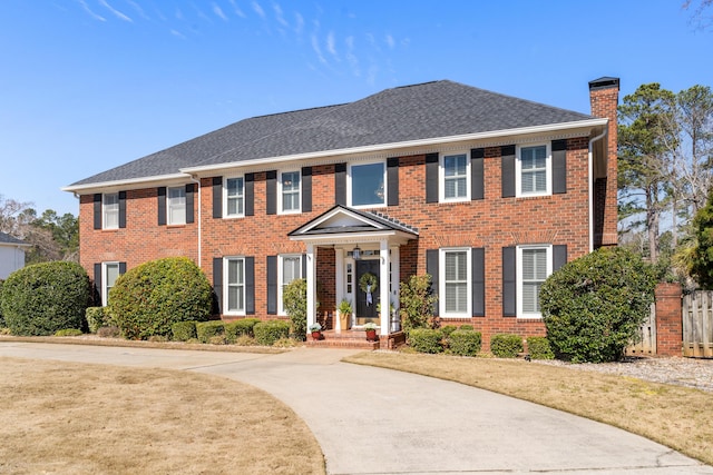 colonial home featuring a shingled roof, brick siding, and a chimney