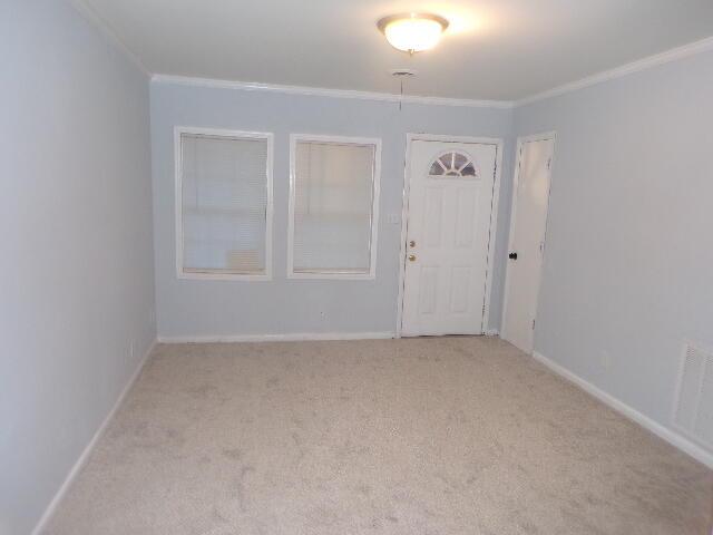 interior space featuring light carpet, visible vents, ornamental molding, and baseboards