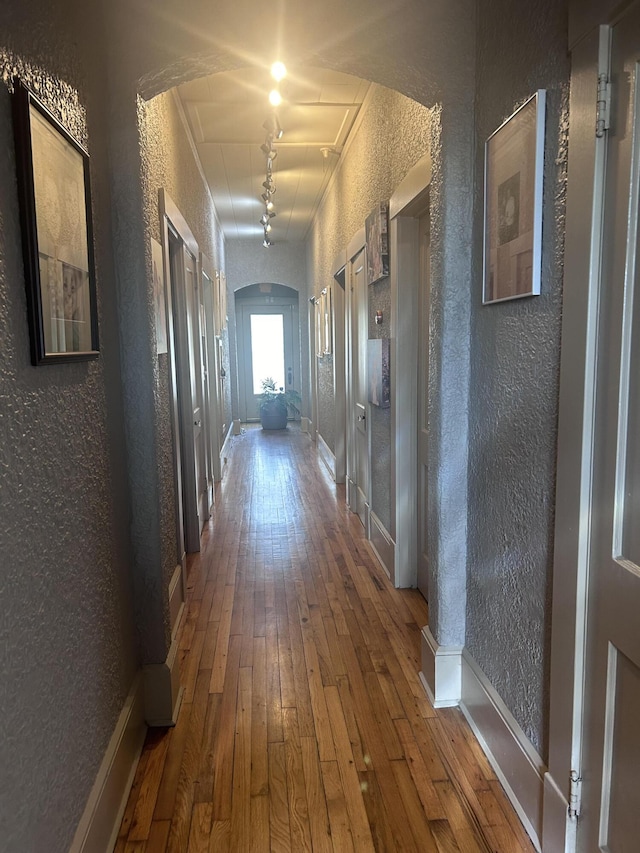 corridor featuring a textured wall, arched walkways, and wood-type flooring