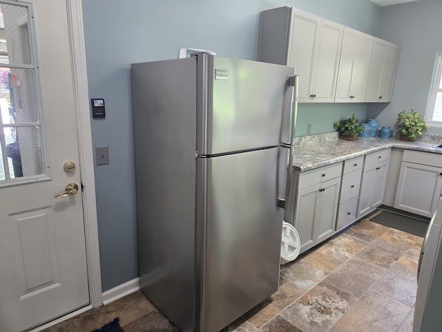 kitchen featuring light stone counters, stone finish flooring, white cabinetry, and freestanding refrigerator
