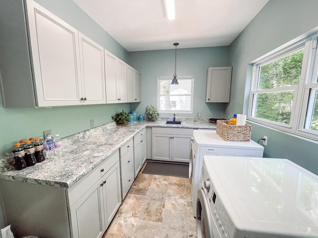 laundry area featuring stone finish flooring, separate washer and dryer, cabinet space, and a sink