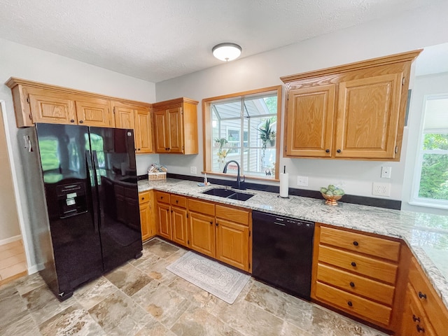 kitchen with a textured ceiling, a sink, stone finish flooring, black appliances, and light stone countertops