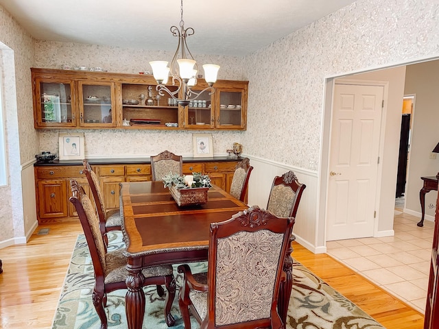 dining space with a chandelier, light wood-type flooring, a wainscoted wall, and wallpapered walls