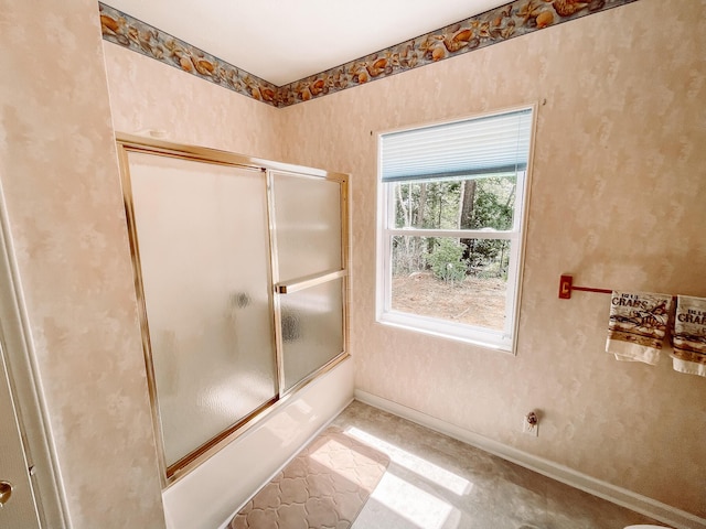 bathroom featuring combined bath / shower with glass door and baseboards