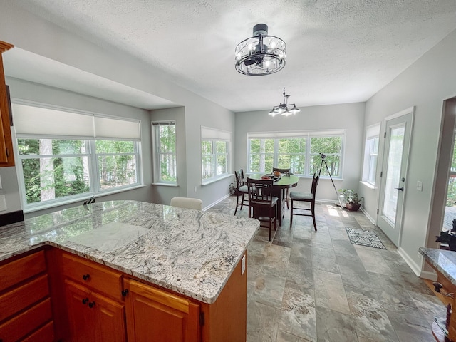 kitchen with stone finish flooring, a notable chandelier, a textured ceiling, and baseboards
