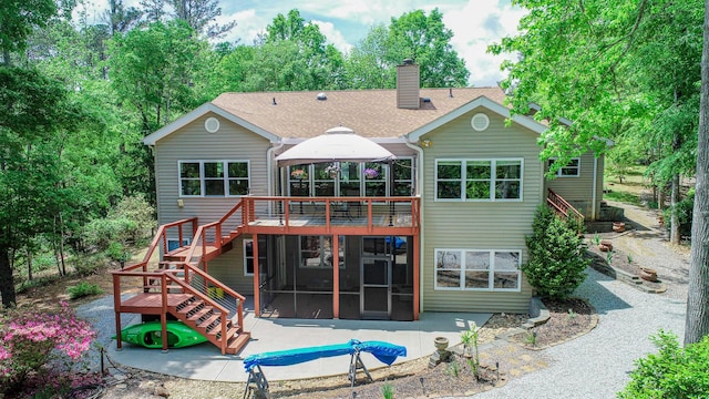 rear view of property featuring a sunroom, stairway, a patio area, a chimney, and a deck