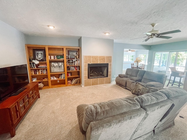 living area with light colored carpet, ceiling fan, a tiled fireplace, and a textured ceiling