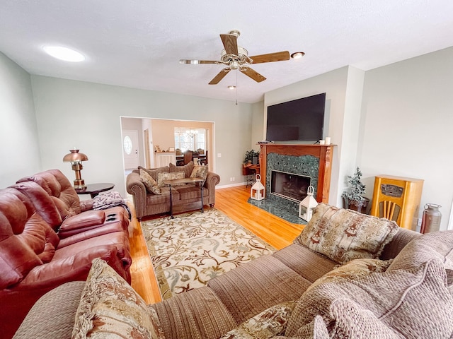 living area featuring a premium fireplace, light wood-type flooring, a ceiling fan, and baseboards