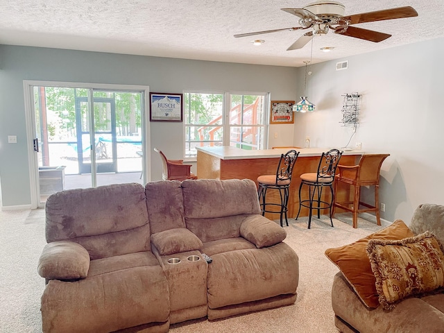 living room with wet bar, visible vents, a textured ceiling, and light colored carpet