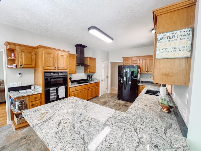 kitchen with light stone countertops, a peninsula, stone finish flooring, black appliances, and wall chimney exhaust hood