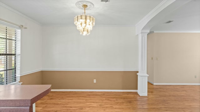 unfurnished dining area featuring baseboards, a notable chandelier, ornamental molding, decorative columns, and wood finished floors