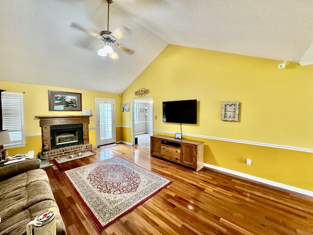 living room featuring ceiling fan, wood-type flooring, a fireplace, and vaulted ceiling