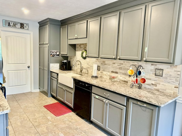 kitchen featuring light stone countertops, backsplash, sink, black dishwasher, and gray cabinets