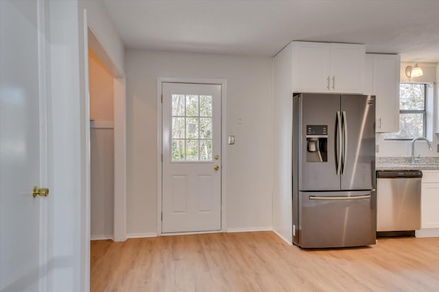 kitchen with light wood-style floors, appliances with stainless steel finishes, white cabinets, and light stone counters