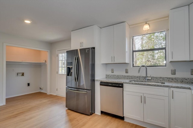 kitchen with light stone counters, stainless steel appliances, light wood-style floors, white cabinetry, and a sink