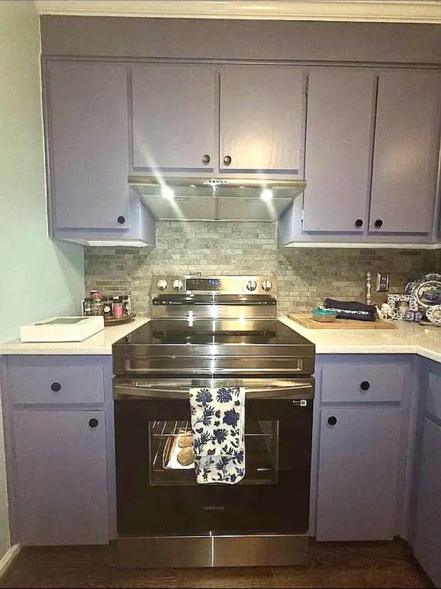 kitchen with electric stove, under cabinet range hood, light countertops, backsplash, and gray cabinetry