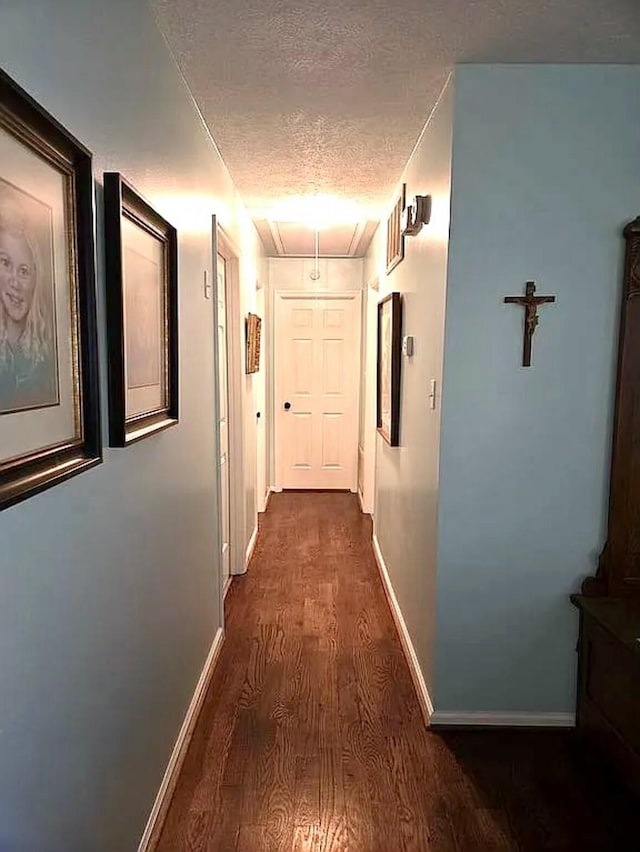 hallway with attic access, baseboards, dark wood-style floors, and a textured ceiling