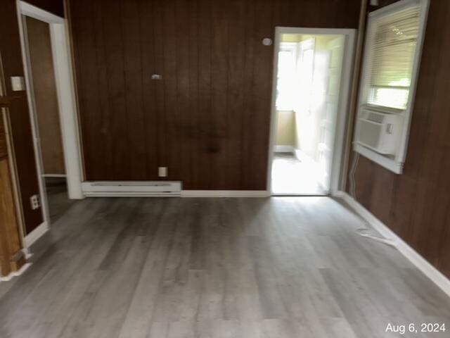 unfurnished room with wood walls, light hardwood / wood-style flooring, and a baseboard radiator