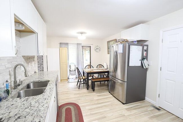 kitchen with sink, stainless steel fridge, white cabinetry, backsplash, and light stone countertops