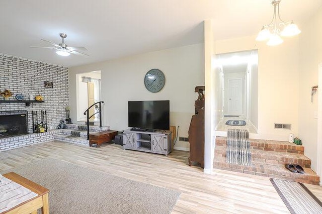 living room with a brick fireplace, light hardwood / wood-style flooring, and ceiling fan