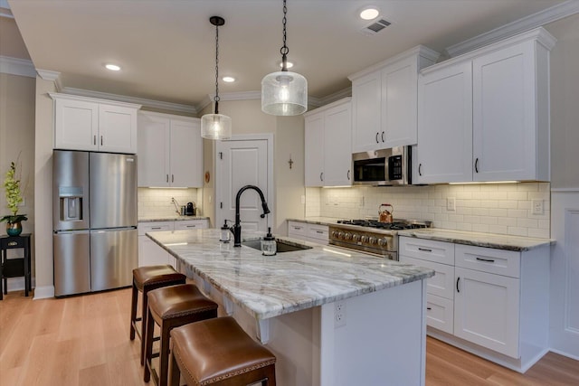 kitchen with stainless steel appliances, a kitchen island with sink, sink, pendant lighting, and white cabinets