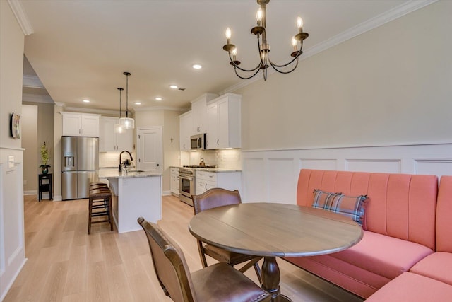 dining room with a chandelier, light wood-type flooring, crown molding, and sink