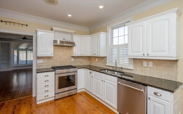 kitchen with dark stone countertops, stainless steel appliances, under cabinet range hood, white cabinetry, and a sink