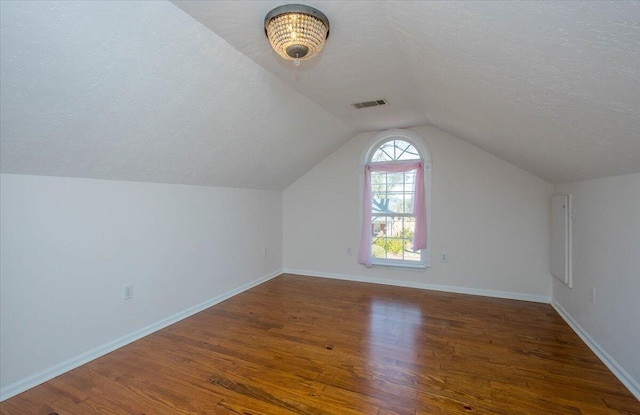 bonus room featuring a textured ceiling, dark wood-style flooring, visible vents, baseboards, and vaulted ceiling