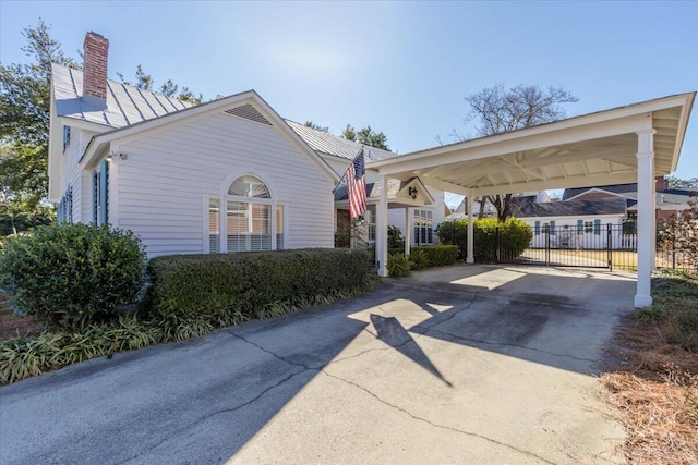 exterior space featuring a chimney, concrete driveway, fence, metal roof, and a carport