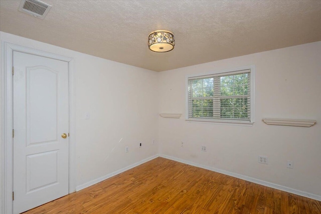 empty room featuring a textured ceiling, wood finished floors, visible vents, and baseboards