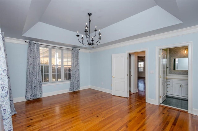 unfurnished dining area with a chandelier, a raised ceiling, crown molding, and wood finished floors