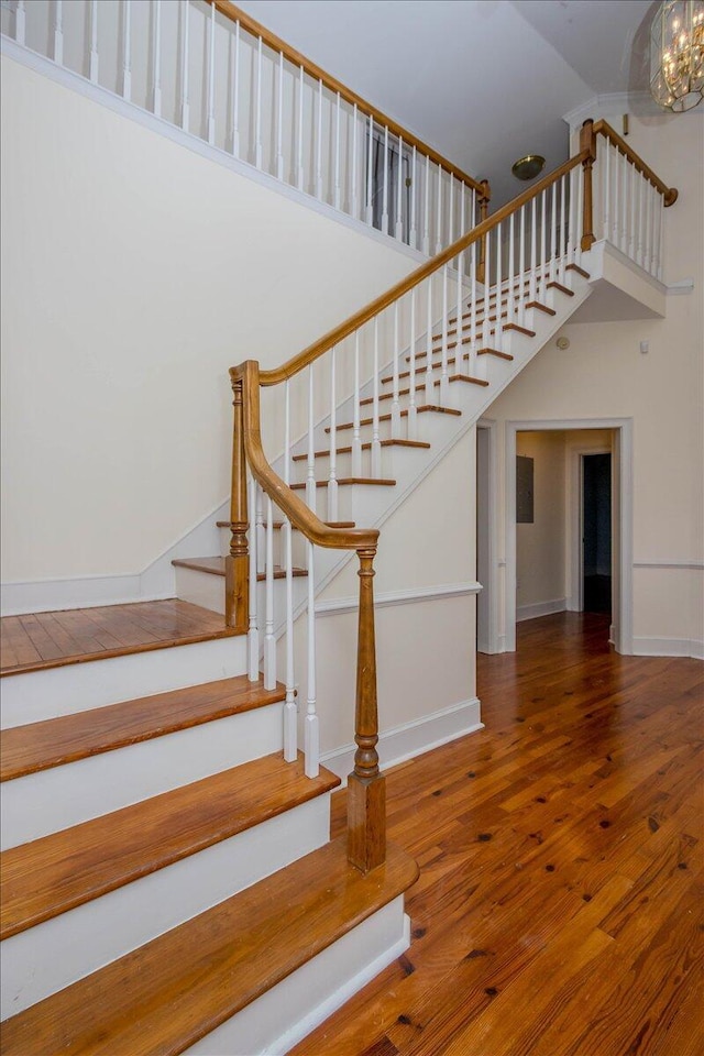 staircase with an inviting chandelier, wood finished floors, a towering ceiling, and baseboards