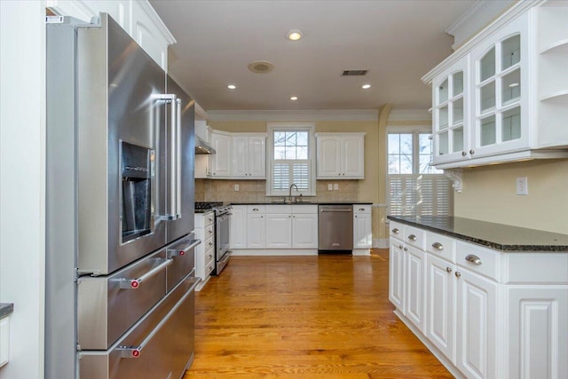 kitchen featuring visible vents, glass insert cabinets, stainless steel appliances, white cabinetry, and a sink