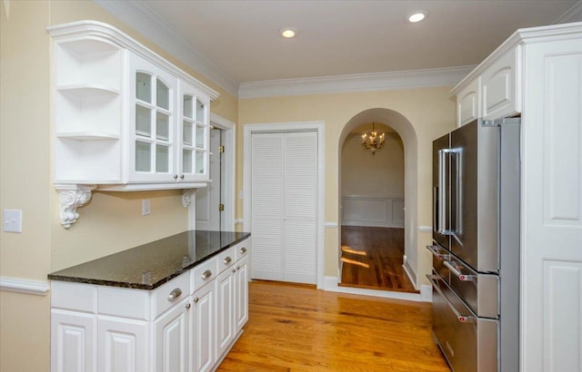 kitchen with arched walkways, light wood-style flooring, high quality fridge, glass insert cabinets, and white cabinetry