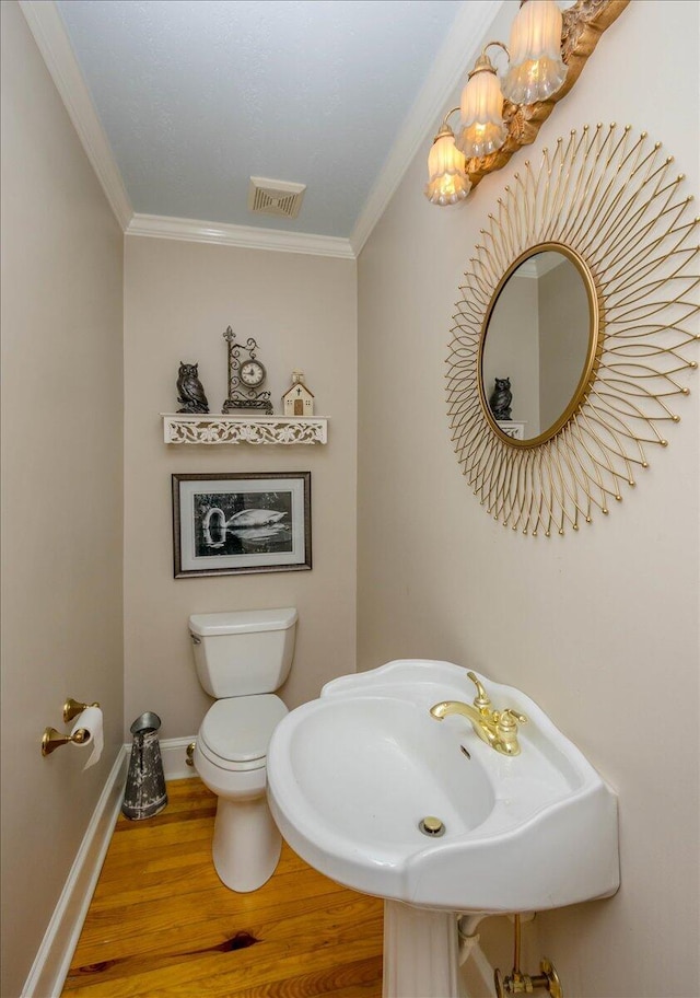 bathroom with baseboards, wood finished floors, visible vents, and crown molding