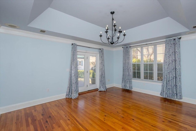 unfurnished room with a notable chandelier, baseboards, a raised ceiling, and wood finished floors