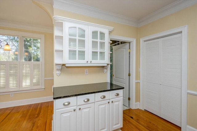 kitchen with crown molding, glass insert cabinets, white cabinets, light wood-type flooring, and dark stone counters