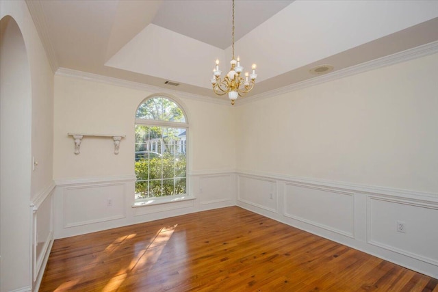 empty room featuring arched walkways, a wainscoted wall, visible vents, ornamental molding, and wood finished floors