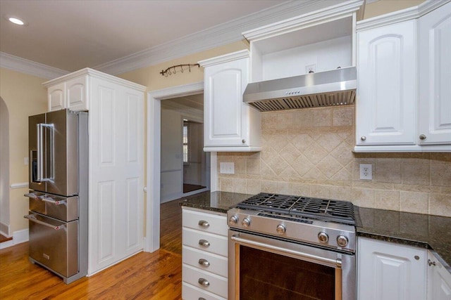 kitchen featuring white cabinets, wall chimney range hood, stainless steel appliances, and dark stone countertops