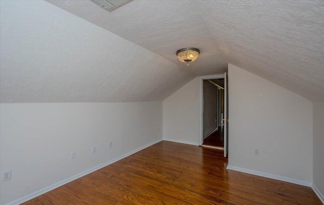 bonus room featuring baseboards, visible vents, dark wood-style flooring, vaulted ceiling, and a textured ceiling