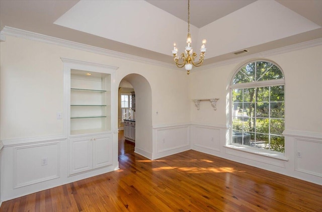 unfurnished dining area featuring visible vents, built in features, arched walkways, dark wood-style floors, and ornamental molding