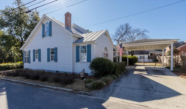 view of side of property with metal roof, fence, concrete driveway, a standing seam roof, and a chimney