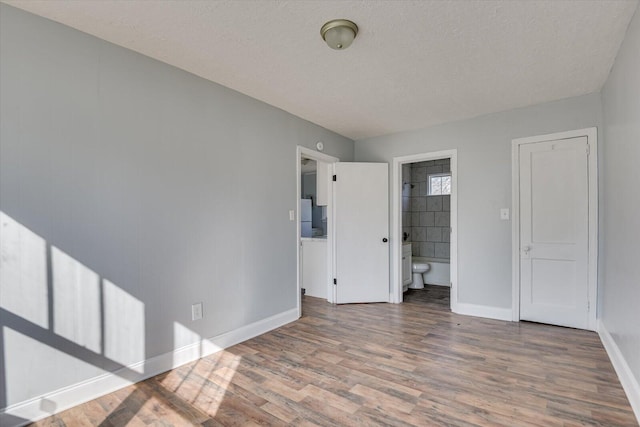 unfurnished bedroom with wood-type flooring, connected bathroom, and a textured ceiling