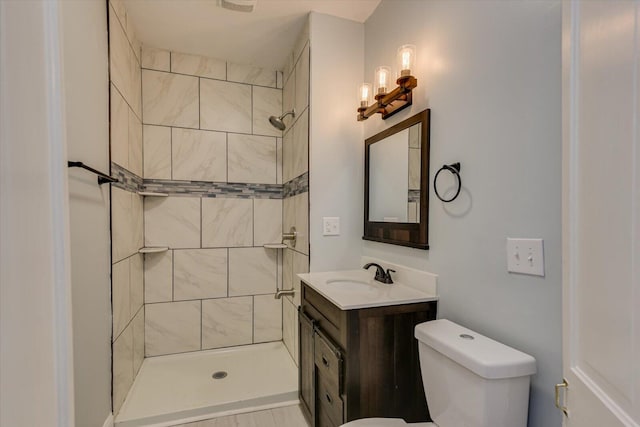 bathroom featuring toilet, a tile shower, and vanity