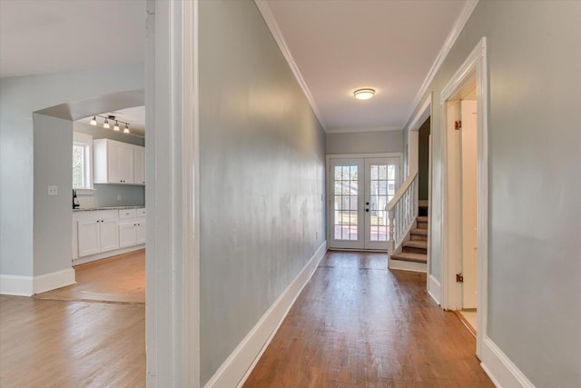 hallway featuring rail lighting, ornamental molding, french doors, and light wood-type flooring