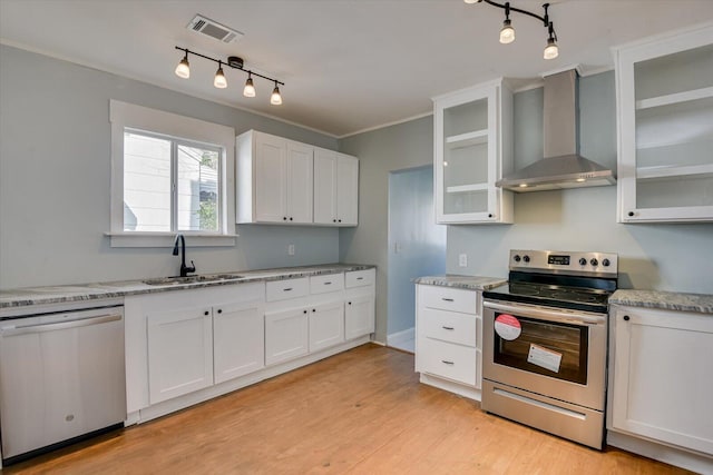 kitchen with wall chimney range hood, sink, white cabinetry, light wood-type flooring, and stainless steel appliances