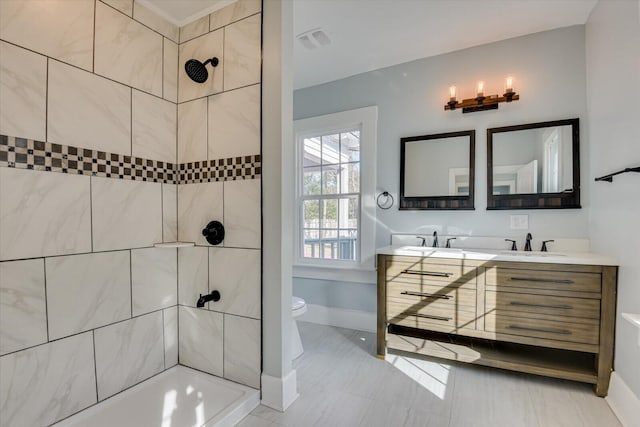 bathroom featuring toilet, a tile shower, and vanity