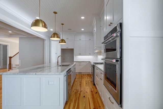 kitchen featuring appliances with stainless steel finishes, a kitchen island with sink, sink, white cabinetry, and hanging light fixtures